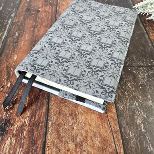 May include: A gray book cover with a repeating pattern of black books and floral designs. The cover has black ribbon bookmarks attached.