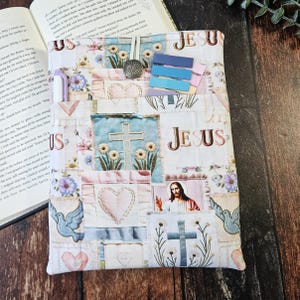 May include: A patchwork book cover with religious imagery. The cover features squares with crosses, hearts, doves, and a picture of Jesus. The word "JESUS" is printed on the cover. Includes a pen, bookmarks, and a decorative metal clip.