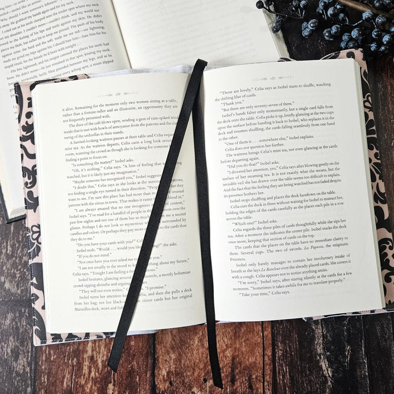 May include: A close-up of an open book with black and white patterned covers. The book is open to a page with text about a woman named Celia and a deck of cards. The text reads, "Those are lovely," Celia says as she shuffles a deck of cards, watching the shining pile of cards."