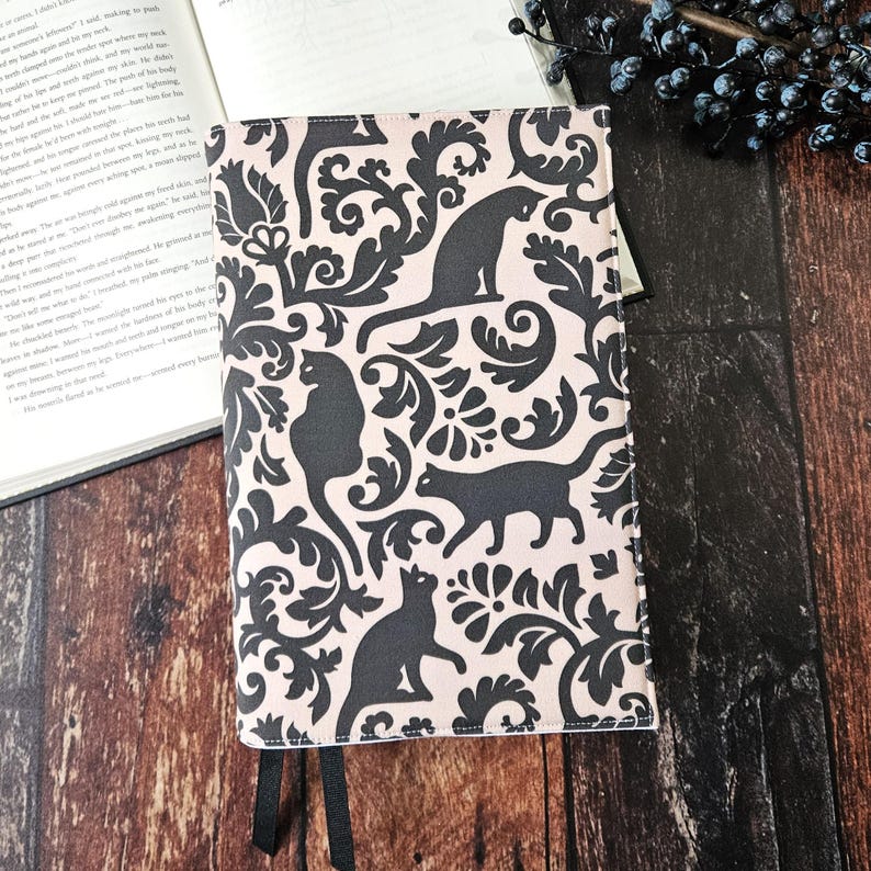 May include: A pink and black book cover with a repeating pattern of black cats and floral designs.