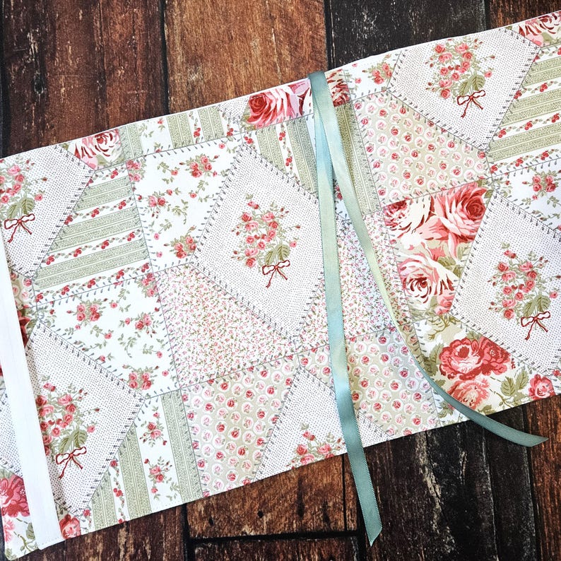 K&ouml;nnte beinhalten: Ein Patchwork-Tischl&auml;ufer mit floralem Design und hellgr&uuml;nem Band. Der L&auml;ufer zeigt rosa und gr&uuml;ne Blumenmuster auf wei&szlig;em Hintergrund. Das Design umfasst Rosen und Schleifen und schafft eine Vintage-&Auml;sthetik.