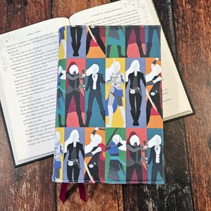 May include: A colorful book cover featuring a repeating pattern of stylized figures in various poses. The figures are outlined in black and filled with vibrant colors like red, blue, and purple. A maroon ribbon bookmark is visible.