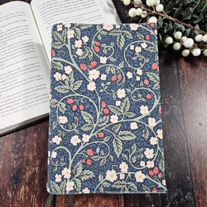 May include: A blue and green floral patterned notebook cover with white flowers and red berries. The cover is made of a durable material and is perfect for protecting your notebook.