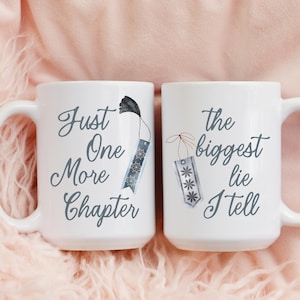 Könnte beinhalten: Zwei weiße Keramikbecher mit schwarzem Text und Aquarell-Lesezeichen-Illustrationen. Auf einem Becher steht "Just One More Chapter", auf dem anderen "The biggest lie I tell". Die Becher haben weiße Griffe und sind vor einem rosa Hintergrund platziert.