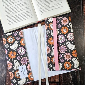 May include: A black book cover with a white background and a pink ribbon. The cover features a repeating pattern of orange, pink, and white flowers with white ghosts. The text "Elizabeth Mayfur Handmade" is printed on the cover.