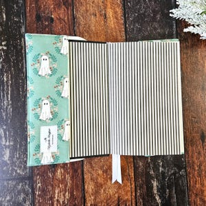 Peut inclure: Une couverture de livre bleu sarcelle avec un fant&ocirc;me blanc et un motif floral. La couverture a une colonne vert&eacute;brale noire et un signet blanc. L'int&eacute;rieur du livre est &agrave; rayures noires et blanches.