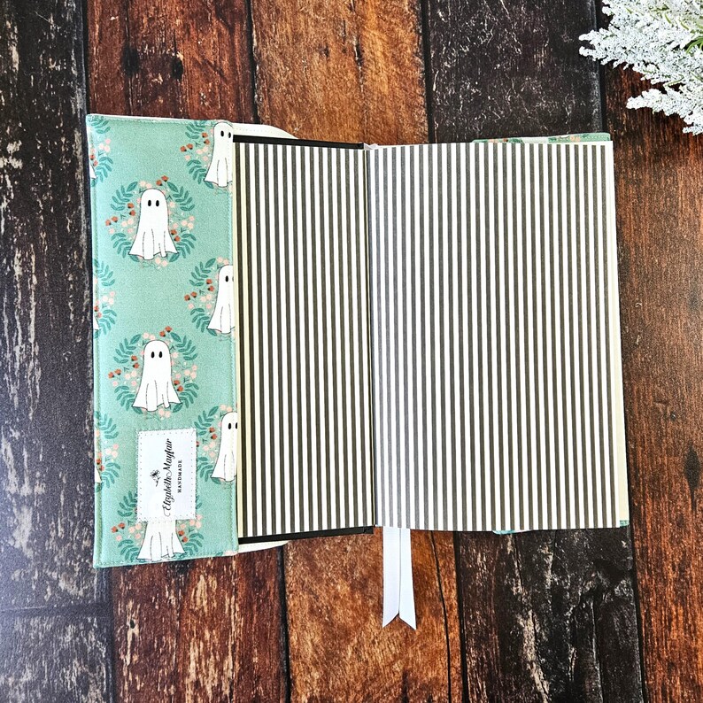 Peut inclure: Une couverture de livre bleu sarcelle avec un fant&ocirc;me blanc et un motif floral. La couverture a une colonne vert&eacute;brale noire et un signet blanc. L'int&eacute;rieur du livre est &agrave; rayures noires et blanches.