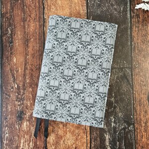 May include: A gray fabric notebook cover with a repeating pattern of open books on a gray background. The cover has two black ribbon bookmarks.