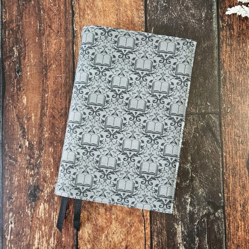 May include: A gray fabric notebook cover with a repeating pattern of open books on a gray background. The cover has two black ribbon bookmarks.