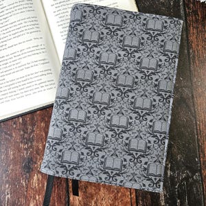 May include: A gray book cover with a repeating pattern of black open books and ornate designs. The cover has two black ribbon bookmarks.