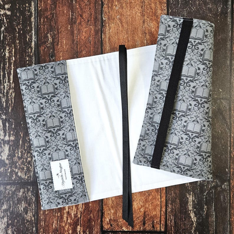 May include: A white book cover with a black ribbon bookmark. The cover has a gray and black pattern of books and floral designs. The text "Elizabeth Mayfair" is printed on the cover.