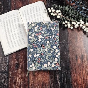 May include: A blue notebook cover with a floral pattern featuring white flowers and red berries. The pattern is reminiscent of a vintage design.