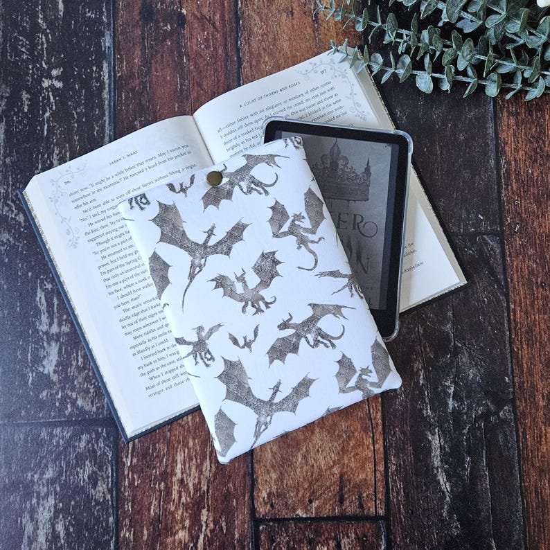 K&ouml;nnte beinhalten: Wei&szlig;e E-Reader-H&uuml;lle mit einem schwarz-wei&szlig;en Drachenmuster. Die H&uuml;lle liegt auf einem Buch mit dem Titel "A Court of Thorns and Roses".