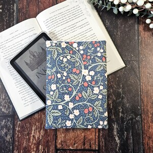 Puede incluir: Una funda de libro azul y verde con un patrón floral con flores blancas y bayas rojas. La funda tiene un cierre de botón.