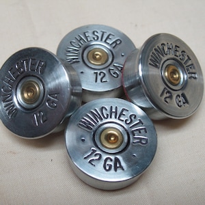 May include: Four silver Winchester 12 GA shotgun shell casings. Each casing has the word "WINCHESTER" and "12 GA" embossed on the top. The center of each casing has a gold-colored primer.