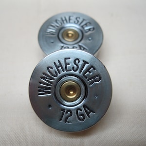 May include: Two silver shotgun shell cufflinks with black lettering that reads "WINCHESTER 12 GA".
