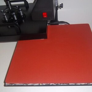May include: A black heat press with a red silicone heat plate. The heat press has a lever and a power switch.