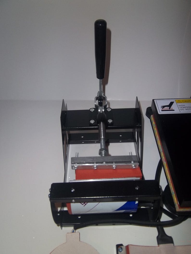 May include: A black heat press with a red heat plate and a lever handle. The heat press is used for transferring designs onto fabric.