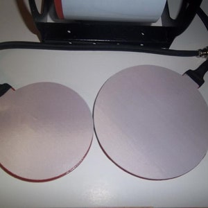 May include: Two round, white heat press pads with red trim, connected to a black cord with a connector on the end.