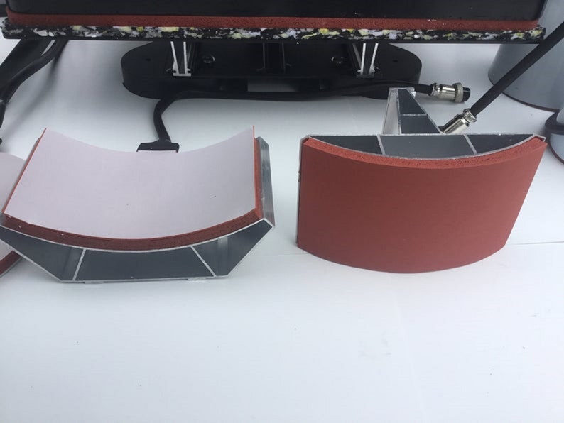May include: Two curved heat press plates, one with a white fabric surface and the other with a red rubber surface. Both plates are made of aluminum and have a silver finish.