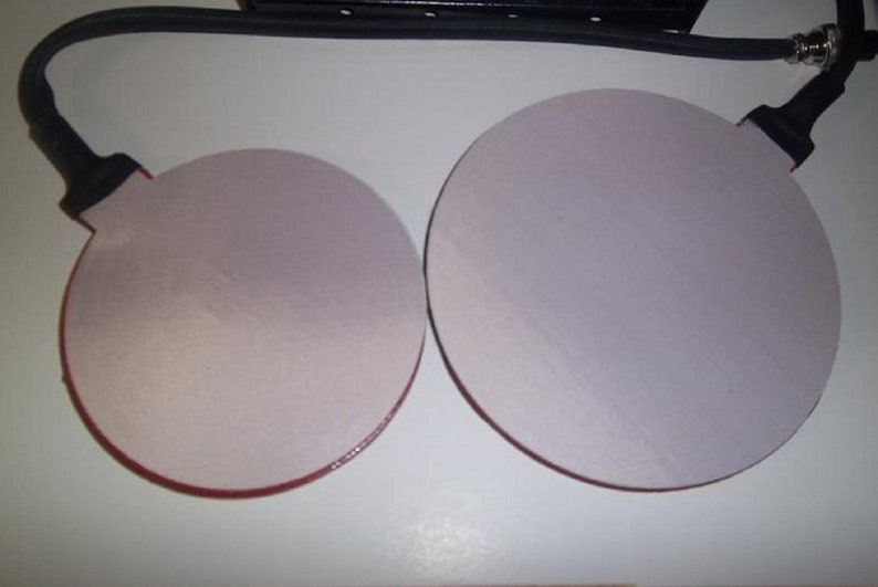 May include: Two round, white, adhesive pads with red edges. The pads are attached to black cords.