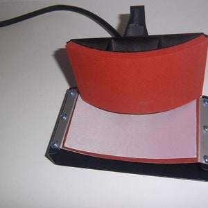 May include: A black heat press with a red silicone pad and a white Teflon sheet. The press is open and ready to use.