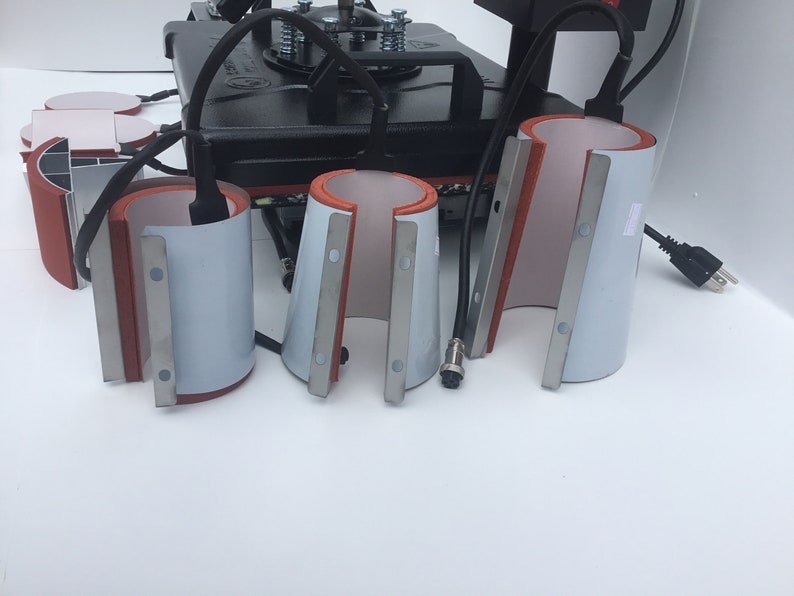 May include: Four white ceramic mug press attachments with red silicone and silver metal accents. The attachments are used for heat pressing designs onto mugs.