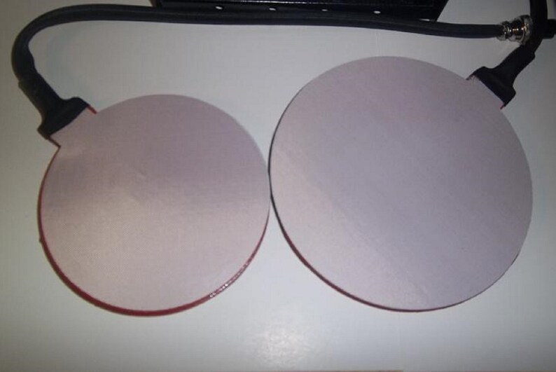 May include: Two round, white, adhesive pads with red edges. The pads are attached to black cords.