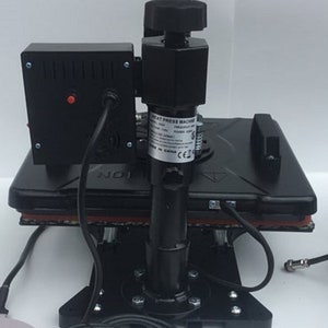 May include: Black heat press machine with a control panel and a lever. The machine is on a black base with a red heat resistant pad. The machine has a label that says "Heat Press Machine" and "Made in China".