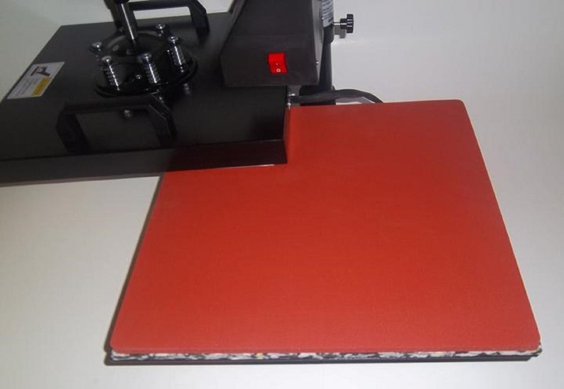 May include: A black heat press with a red silicone heat plate. The heat press has a lever and a power switch.
