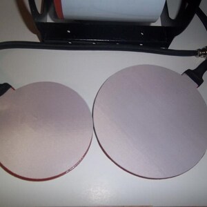 May include: Two round, white heat press pads with red trim, connected to a black cord with a plug.