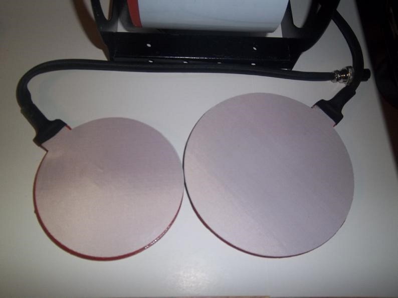 May include: Two round, white heat press pads with red trim, connected to a black cord with a plug.