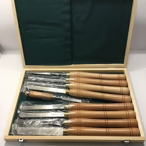 May include: A set of ten wood carving tools in a wooden box with a green felt lining. The tools have wooden handles and are arranged in rows. The tools are labeled with numbers.