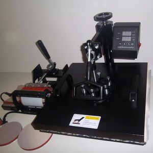 May include: Black heat press machine with a digital display and a lever for pressing. The machine has a round base and a rectangular platform. The platform has a white surface and a black border. The machine is on a white surface.