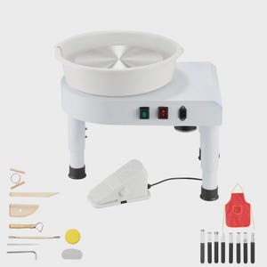 May include: A white electric pottery wheel with a circular metal plate, a foot pedal, and a set of sculpting tools. The machine features a green power switch, a red toggle switch, and a power port. Included are wooden and metal tools, a red apron.