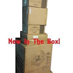 May include: A stack of brown cardboard boxes with the word "INKSTAR" printed on them. The boxes are stacked on top of each other and the top box has a picture of a pinball machine on it. The text "New In The Box!" is printed in red letters on the front of the boxes.