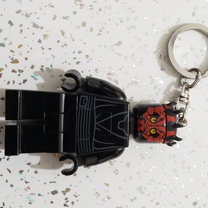 May include: Black Lego minifigure keychain with a red Darth Maul head. The keychain features a silver metal ring.