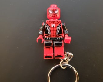 May include: A red and black Spider-Man Lego figure attached to a silver keyring. The figure has a detailed design with a spiderweb pattern on the torso and a mask with white eyes. The keyring is a standard size.