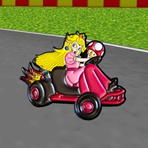 Pu&ograve; includere: Un personaggio dei cartoni animati rosa e nero che guida un kart rosso e nero con fiamme che escono dalla parte posteriore. Il personaggio ha i capelli biondi e una corona. Il kart ha un fungo nella parte anteriore.