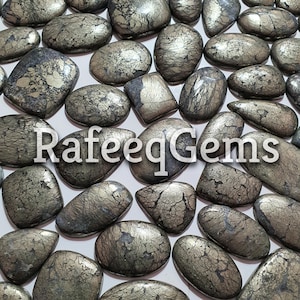 Könnte beinhalten: Eine Sammlung von 25 natürlichen Pyrit-Cabochons, jeder mit einem einzigartigen, komplizierten Muster aus silbernen und goldenen Adern. Die Cabochons sind glatt und poliert, in verschiedenen Formen und Größen. Die Steine sind auf einem weißen Hintergrund angeordnet.