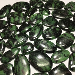 Könnte beinhalten: Eine Sammlung von grünen und schwarzen Edelstein-Cabochons. Die Steine sind glatt und poliert, in verschiedenen Formen und Größen.