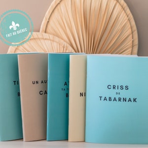 May include: A collection of five notebooks in various colors, including light blue, beige, and cream. Each notebook has text printed on the cover in black. The notebooks are arranged in a row, with a decorative fan in the background.