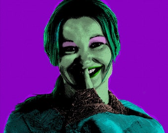 May include: A woman with green skin and pink eyeshadow smiles with her finger covering her mouth. She is wearing a teal and brown patterned shirt.
