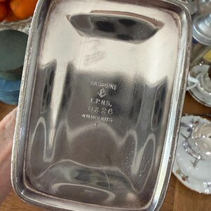 May include: A rectangular silver-colored tray with rounded corners. The tray has a slightly raised rim and a handle-like indentation on one side. The bottom of the tray is stamped with the words "PAIRPOINT", "E.P.N.S.", "0826", and "WM.MOUNTS".