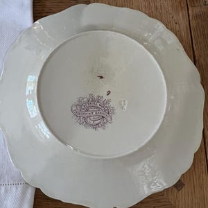 May include: A white ceramic plate with a scalloped edge. The back of the plate has a purple and white design with the text "Samuel Moss, Original, Patent Gardens, Miller & Co."