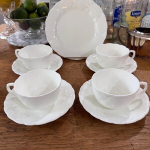 May include: A white porcelain tea set with a large plate, four teacups, and saucers. The set features a delicate embossed leaf pattern. The teacups have handles and sit on matching saucers. The plate is in the center.