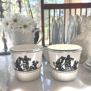 Puede incluir: Dos tazas de cerámica blanca con imágenes en silueta negra de músicos tocando instrumentos. Las tazas tienen un borde blanco y una banda negra alrededor de la parte superior.