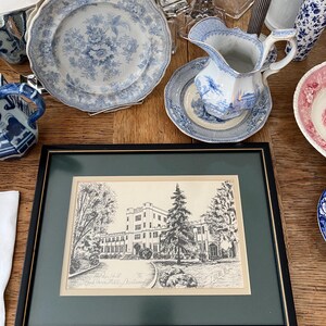 Op de afbeelding: Een zwart ingelijste print van een zwart-witte tekening van een gebouw met een grote boom ervoor. De print is getiteld "Parker Hall - Davidson College" en is gesigneerd "1908".