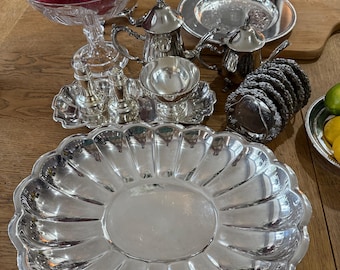 May include: A collection of silver-plated tableware including a large scalloped serving tray, a teapot, a creamer, a salt and pepper shaker set on a rectangular tray, a small bowl, a stack of coasters, and a crystal fruit bowl with pomegranates.