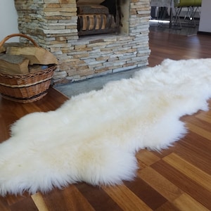 Pode incluir: Um tapete de pele de carneiro branco com pelo longo e felpudo. O tapete está colocado sobre um piso de madeira em uma sala de estar.